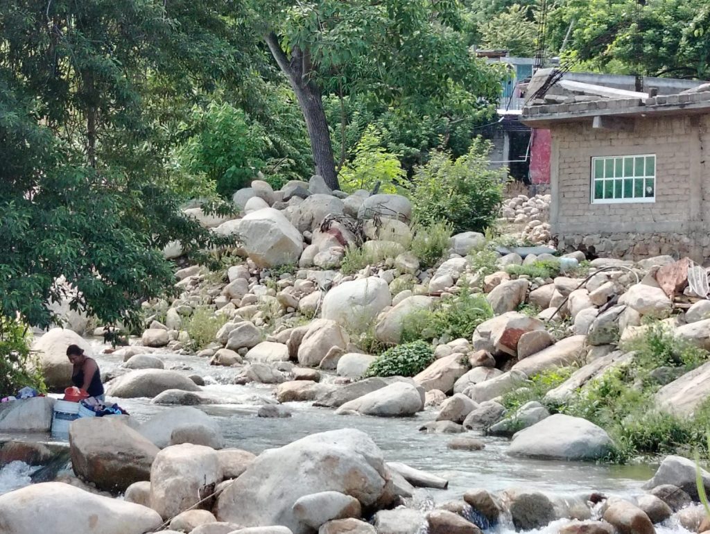 Image shows a woman drying clothes on large rocks next to a river